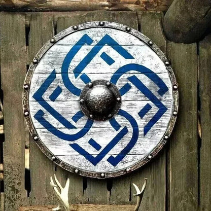 24-inch Viking medieval round shield featuring battle-worn distressed white painted wood with blue interwoven Celtic knot design – weathered steel rim with riveted studs and dark forged iron center boss – rustic wall décor mounted on aged wooden fence with deer antlers below