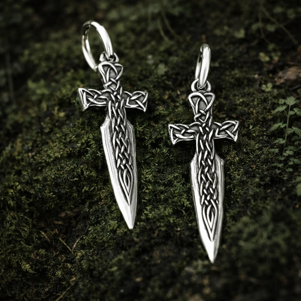 Pair of Viking Celtic Cross Blade Drop Earrings with intricate knotwork, resting on mossy forest ground.