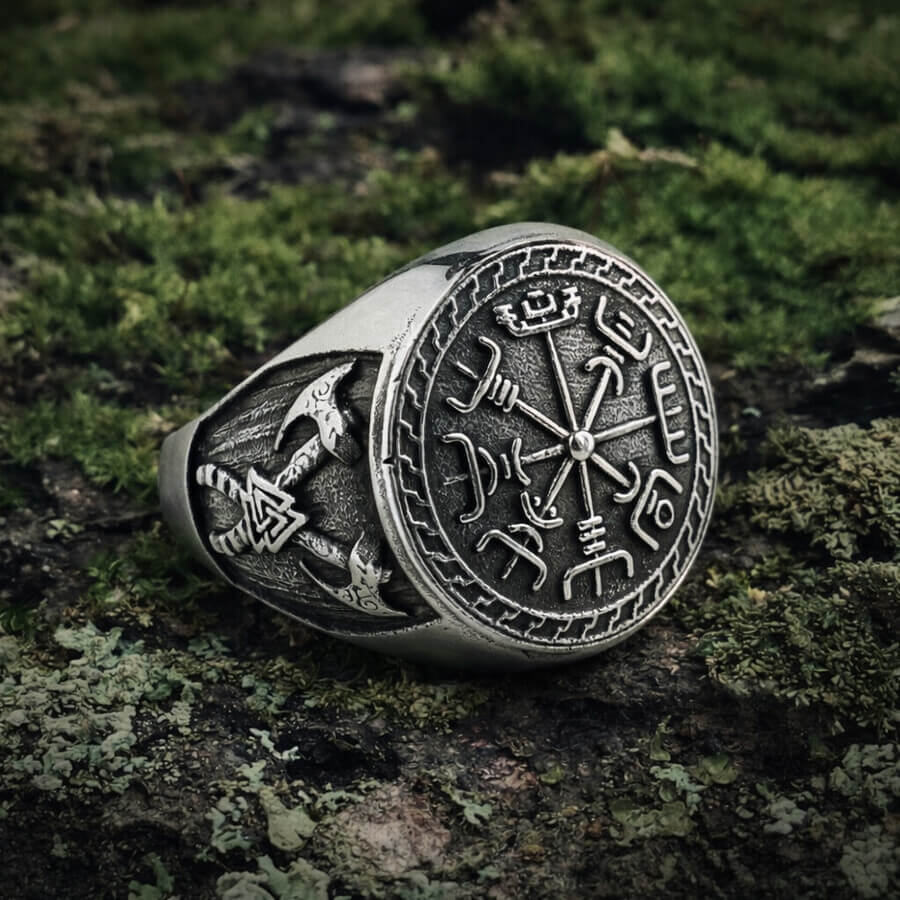 Close-up of a Viking Compass Double Axe Totem Ring with Norse runes and axe carvings resting on mossy ground.