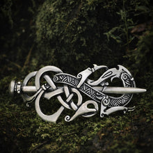 Silver Viking dragon knot hair clip with intricate Norse patterns, resting on lush green moss in soft natural light.