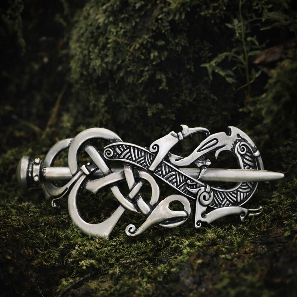 Silver Viking dragon knot hair clip with intricate Norse patterns, resting on lush green moss in soft natural light.
