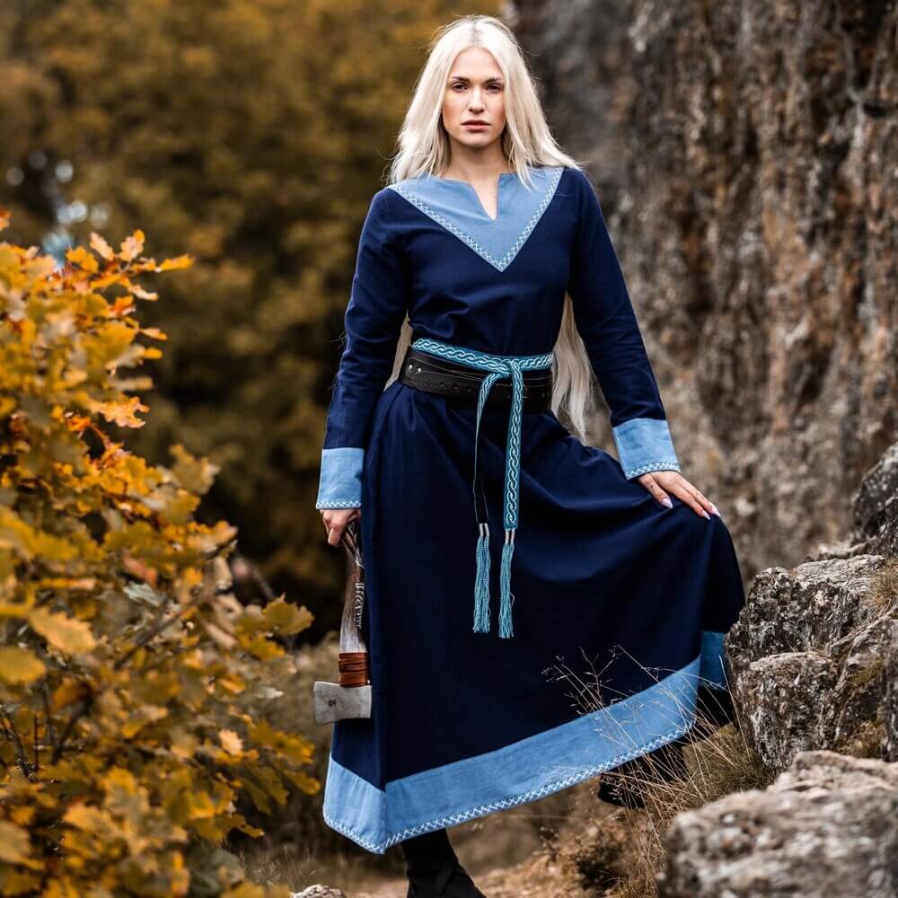 Woman wearing Viking Dress - Dark Blue with LightBlue trim, long gown with pale blue cuffs and hem, standing on rocky forest path.