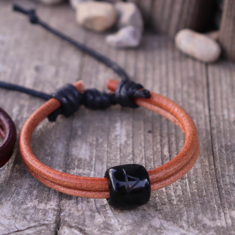 Handmade Viking Horn Rune Leather Bracelet in orange with black rune bead, styled on rustic wooden background.