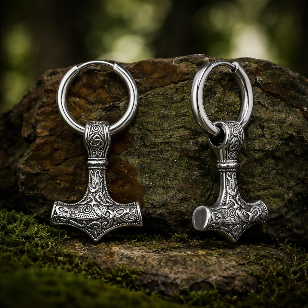Intricately detailed Viking Mjolnir hammer drop earrings rest on mossy stone with forest background.