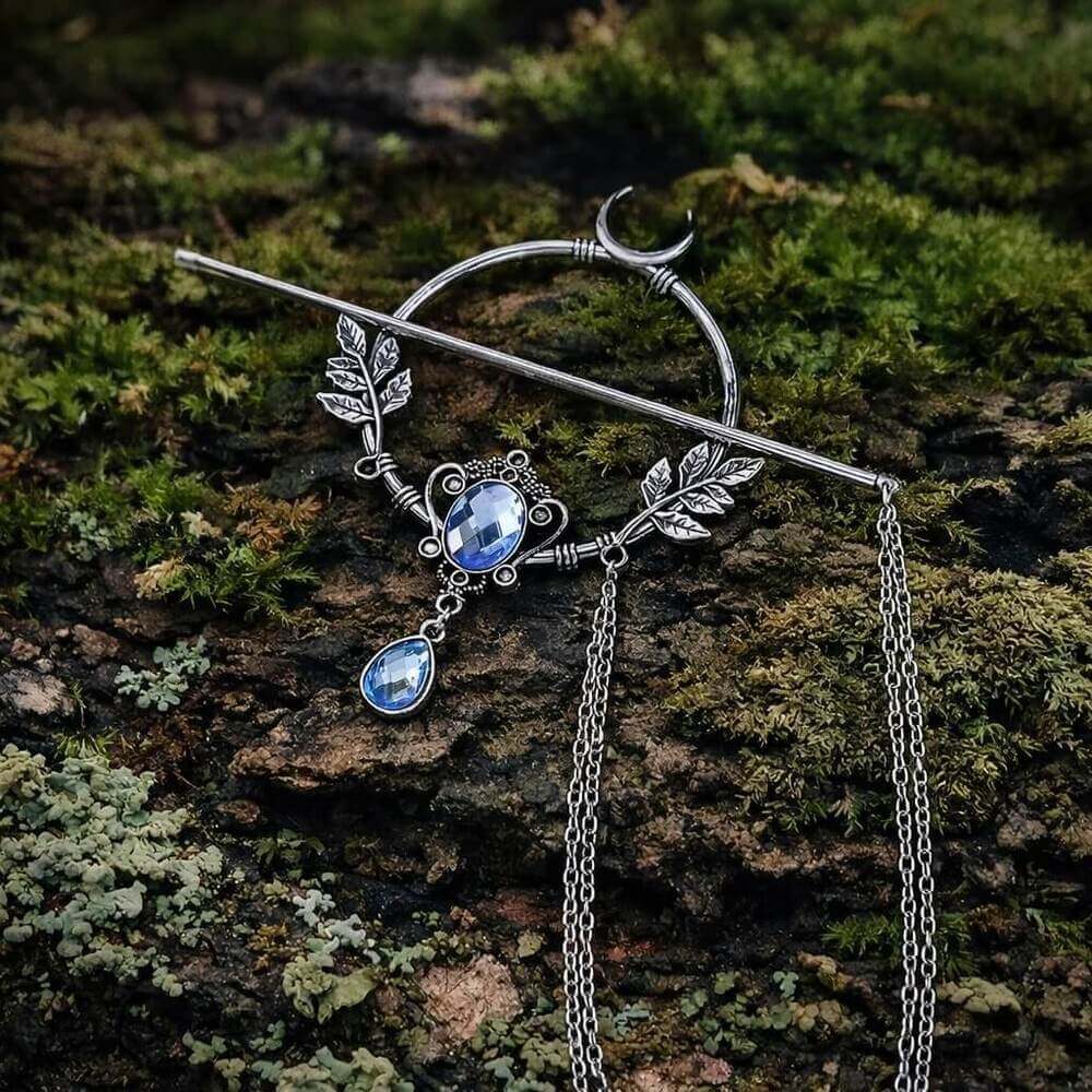 Viking Moonleaf Chain Hair Clip with blue gemstones, crescent moon, and leaf accents, resting on mossy bark.