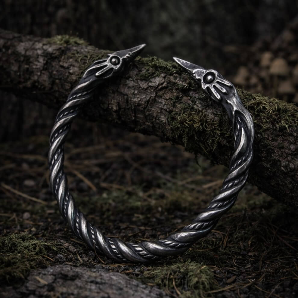 Viking raven head bracelet, antique silver-tone twisted metal, resting on mossy wood.