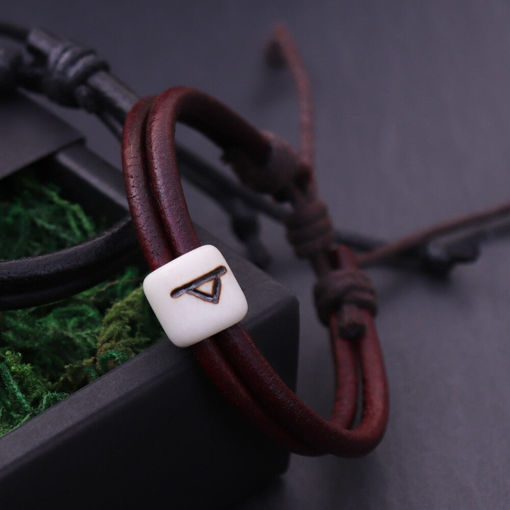 Viking Rune Protection Bracelet with leather cords and bone rune bead draped over a black gift box with green moss.