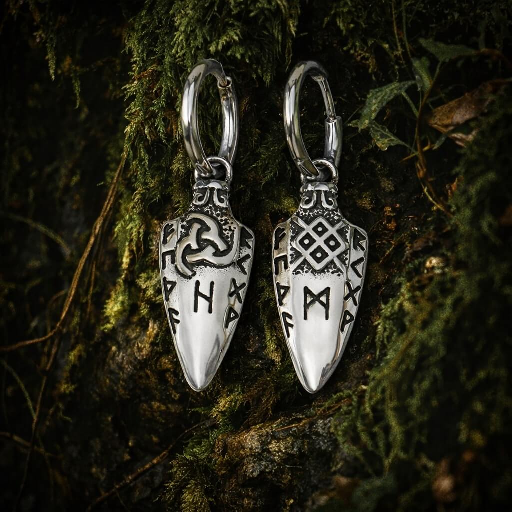 Viking rune spearhead drop earrings with Norse symbols rest against mossy bark in a moody forest scene.