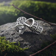 Two silver Viking Rune Spiral Wrap Beard Beads with engraved runes resting on a mossy stone outdoors.