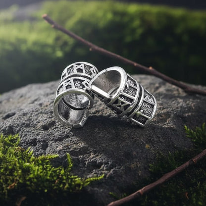Two silver Viking Rune Spiral Wrap Beard Beads with engraved runes resting on a mossy stone outdoors.