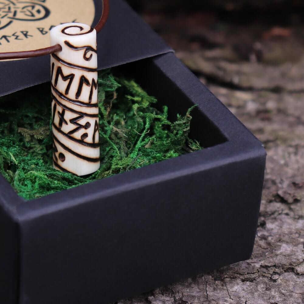 Viking Runic Bone Roller Pendant Necklace on Leather Cord resting in black gift box with green moss.