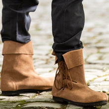 Person standing on cobblestones wearing Viking Sigurd brown suede boots with soft fold-over tops and side laces.