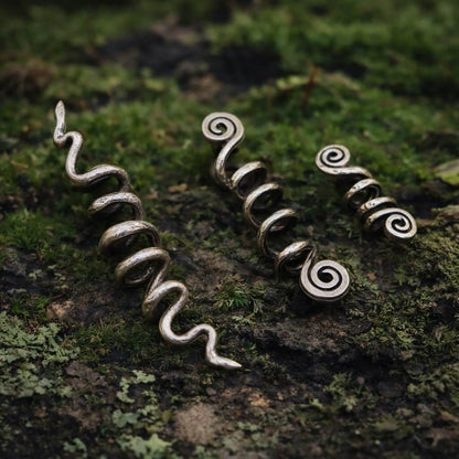 Viking spiral hair beads: three silver-toned metal coils on mossy bark.