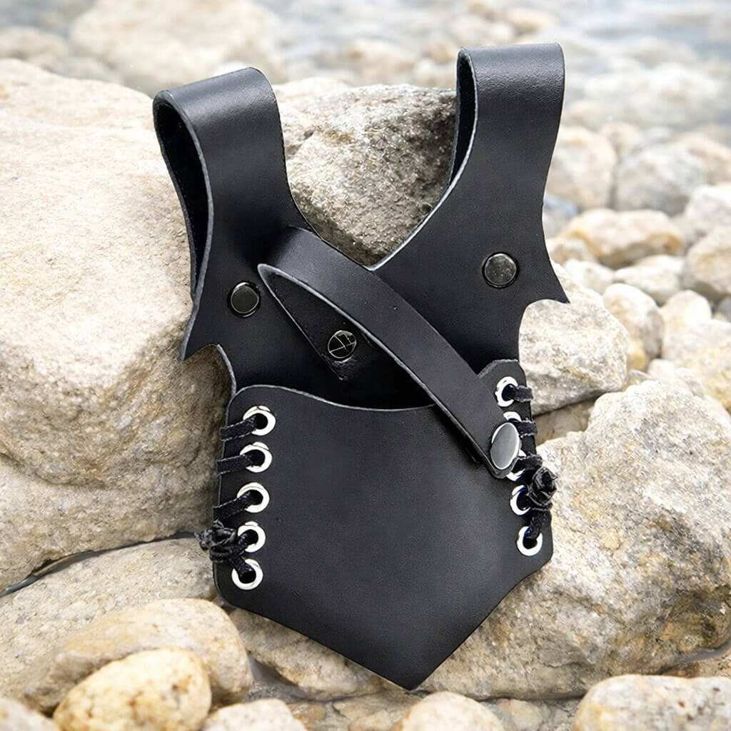 A black leather Viking sword belt hanger with metal rivets rests on pale river stones beside gently flowing water.
