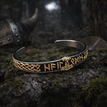 Close-up of a Viking Thor hammer runic cuff bracelet with gold Norse symbols on black metal, resting on mossy stone.