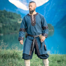 Man wearing Viking Tunic - Blue with Ornate Leather Trim, laced collar and leather cuffs, standing by mountain lake.