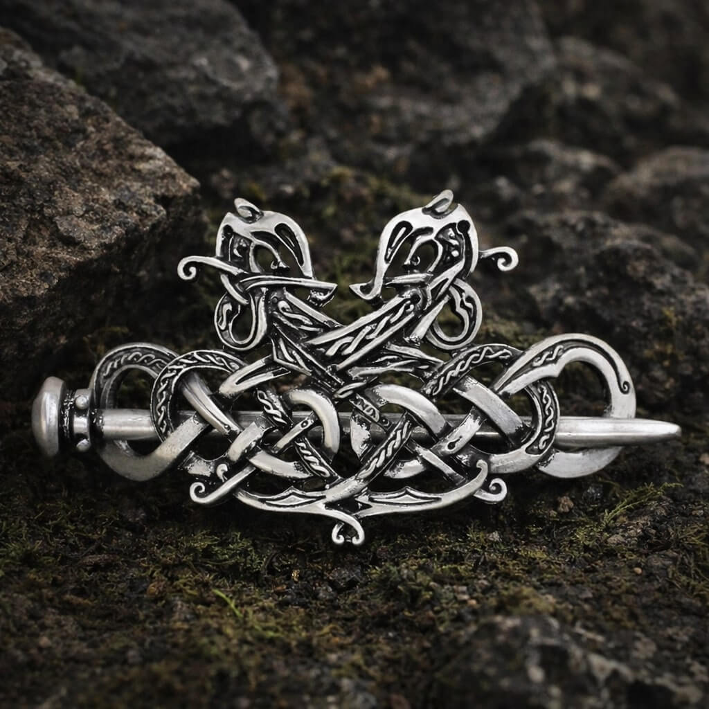 Viking silver twin dragon knotwork hair clip with a pin closure, resting on mossy rocks.