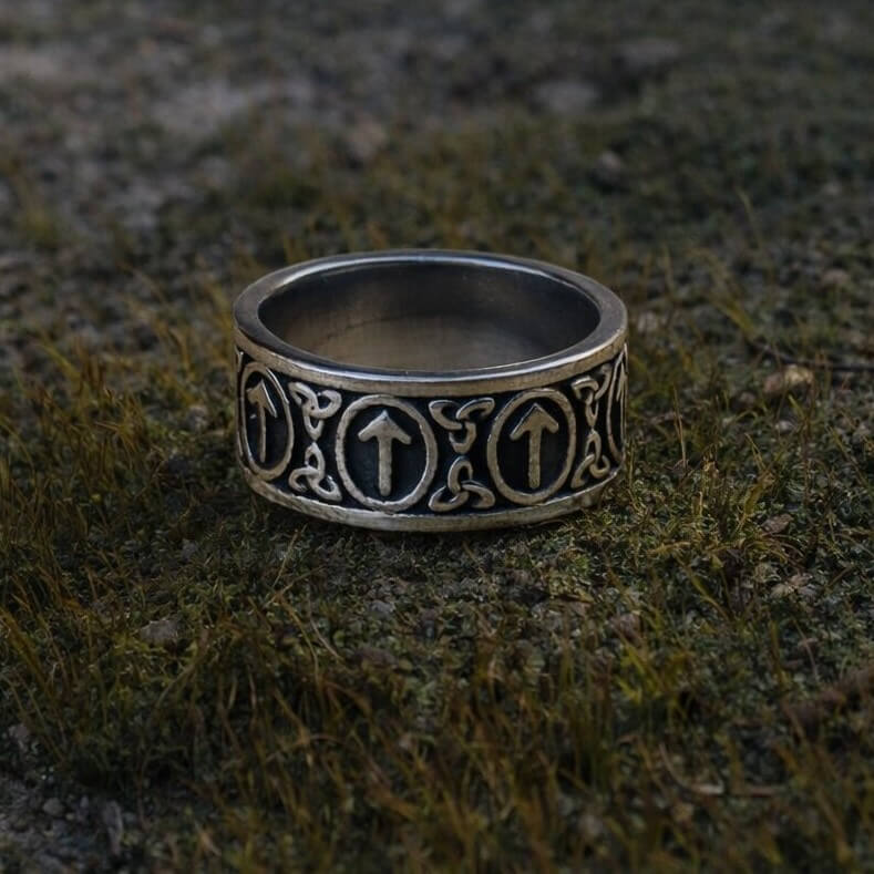 Viking Tyr Rune Band Ring in silver with repeating upward Tyr symbols and intricate Nordic knotwork on mossy ground