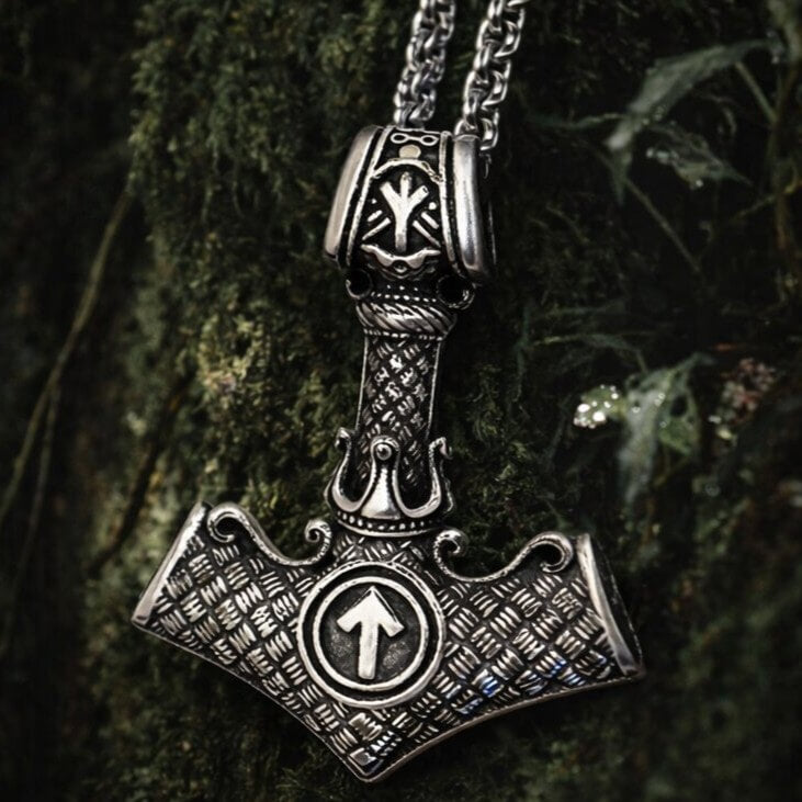 Viking Tyr Rune Thor's Hammer Necklace in silver, engraved Mjolnir pendant with arrow rune on mossy tree bark.