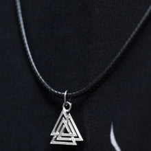 Viking silver Valknut pendant on a black braided cord, against a dark background.