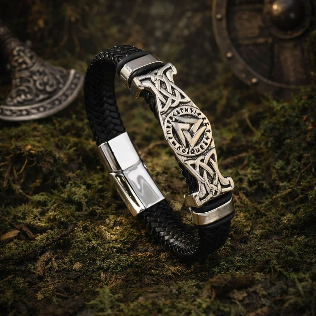 Close-up of a Viking Valknut Rune Braided Leather Bracelet with silver accents, resting on mossy ground.