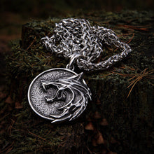 A Viking wolf head necklace in stainless steel lies coiled on a mossy tree stump, showcasing bold Norse jewelry design.